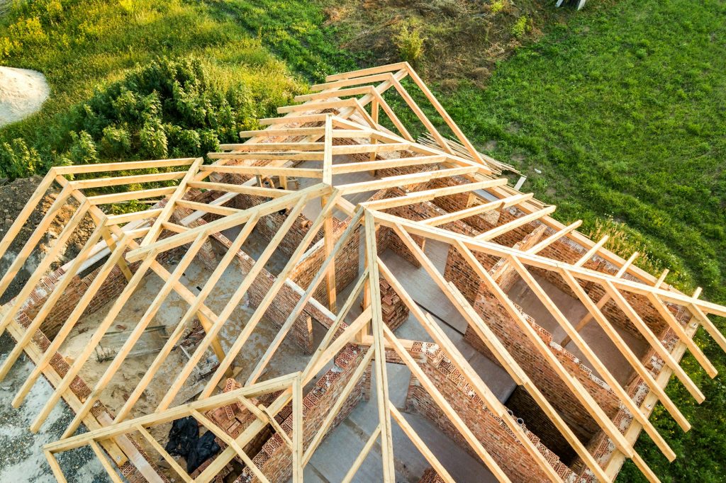 Aerial view of unfinished brick house with wooden roof structure under construction.